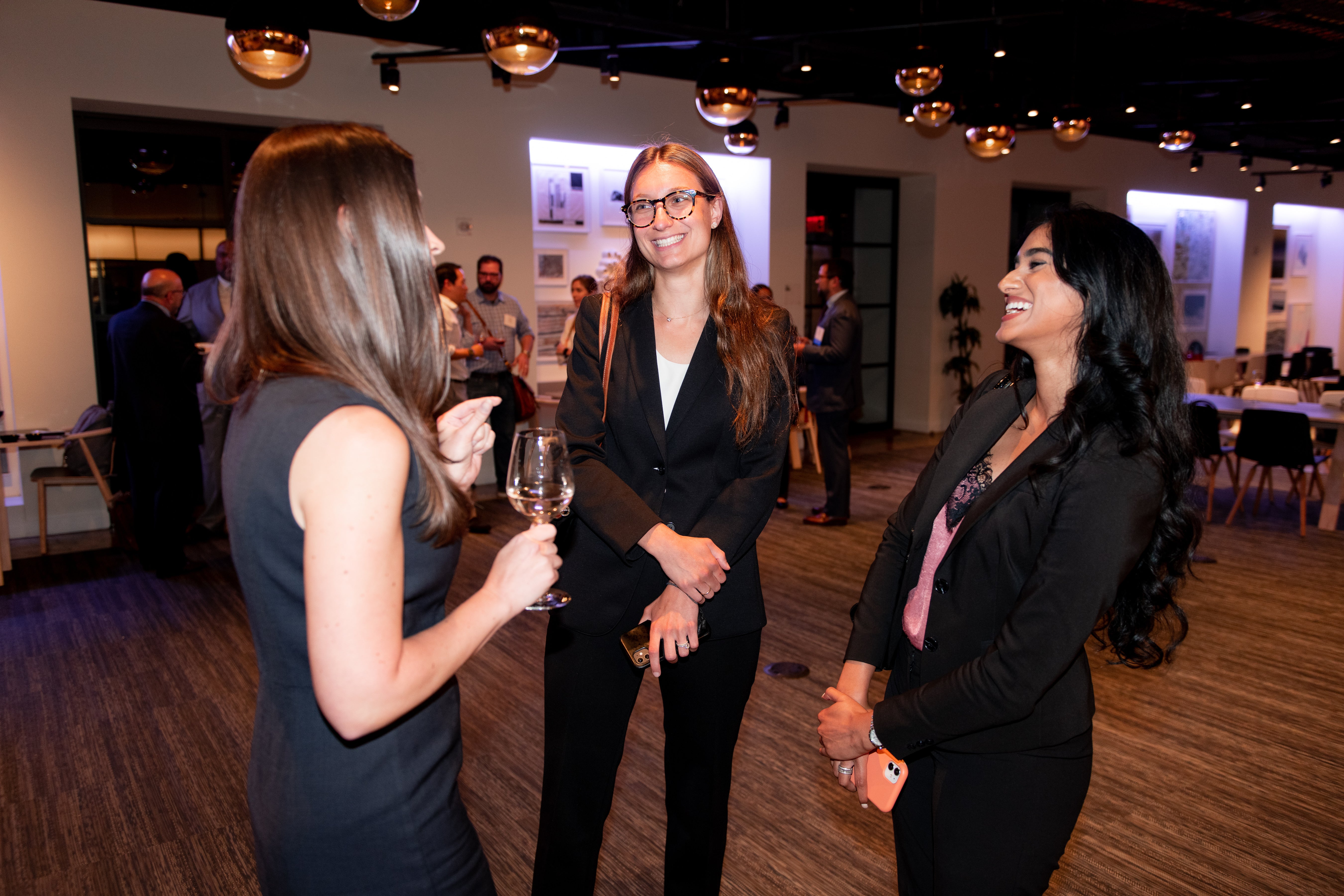 Three women networking, engaging in conversation, and smiling at one another. 