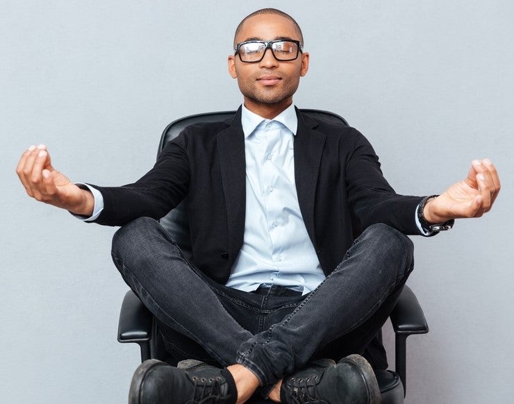 brown-skinned looks-like man, in business cas clothes, meditating on office chair
