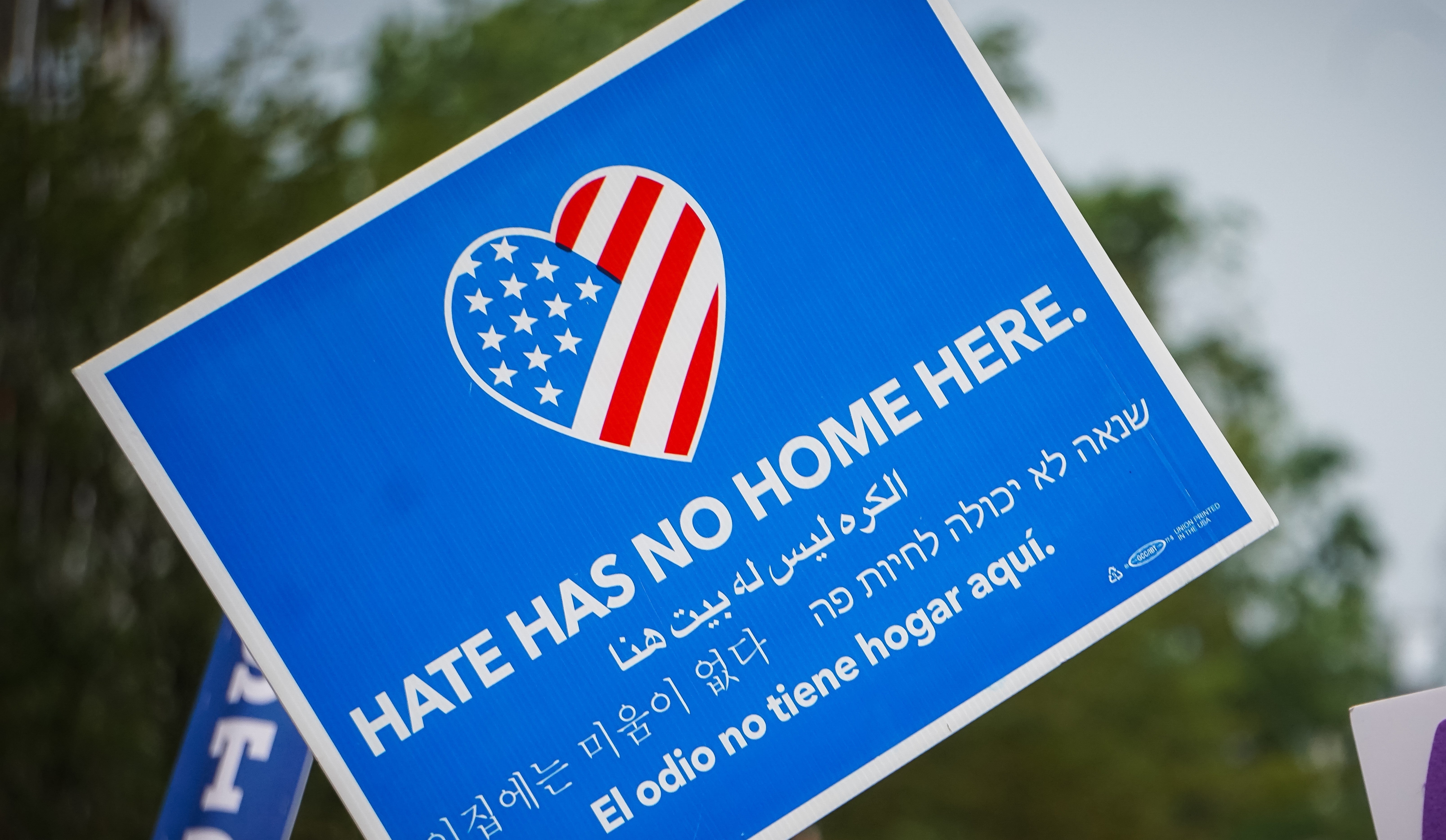 Hate Has No Home Here small poster, looks like is being waved, also, below, in Hebrew, Spanish, and two other languages.