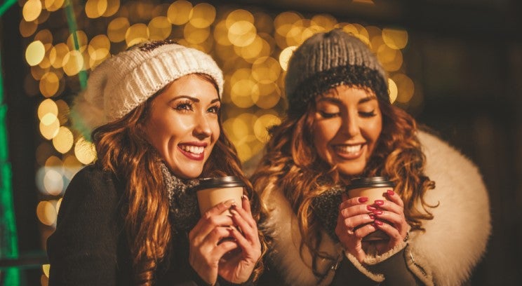 two women wearing winter clothes and holding hot beverages