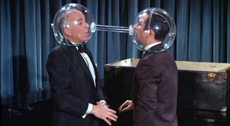 two men with plastic globes over their heads. they are facing one another and the globes are connected with a tube