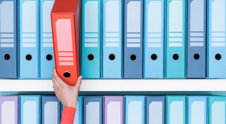 a hand choosing a red file from a shelf of blue files