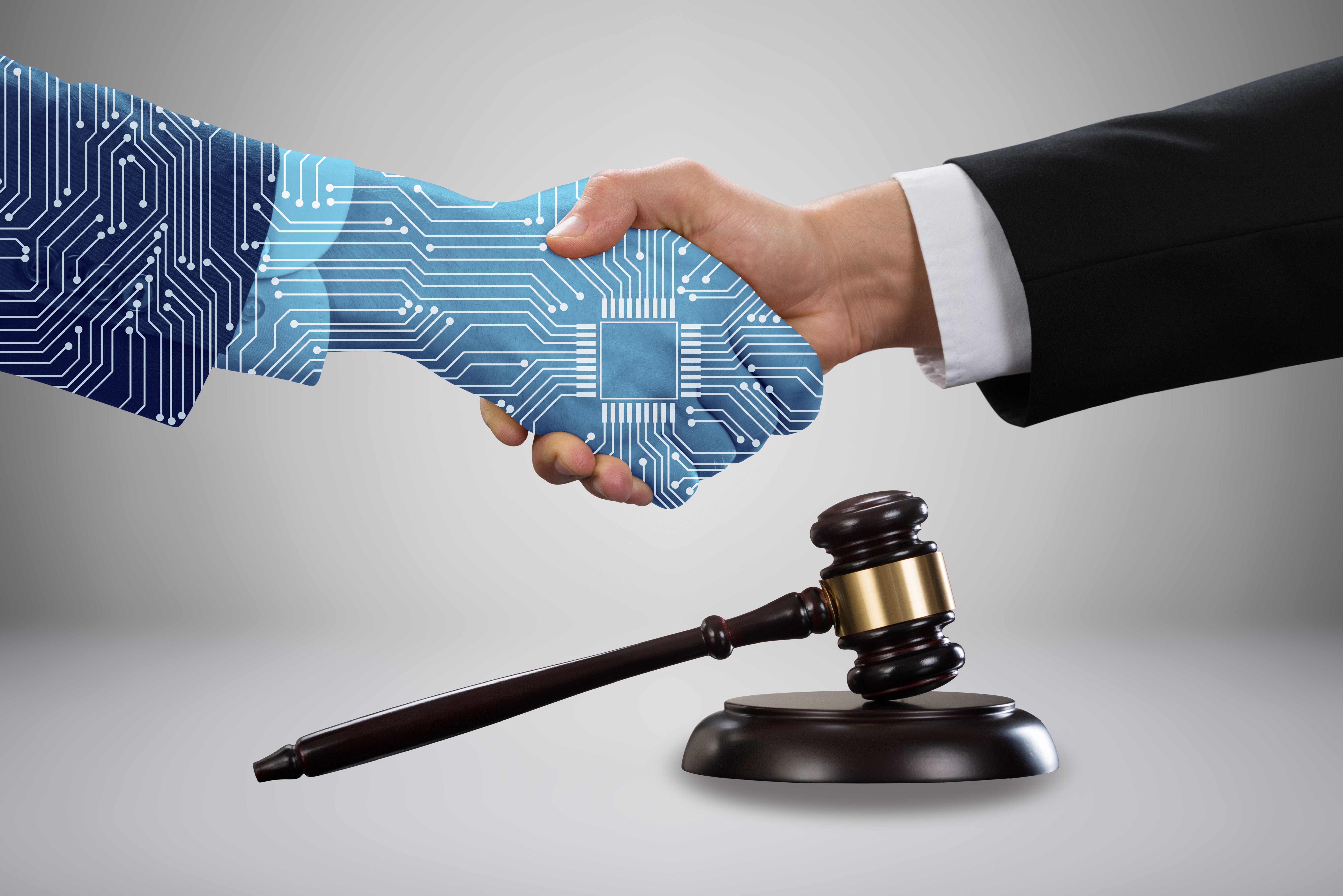 Gavel and mallet in front of lawyer shaking hands with AI partner.