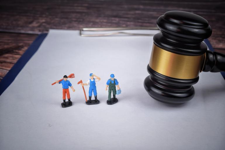 Three miniature toy workers on a clipboard next to a gavel.  