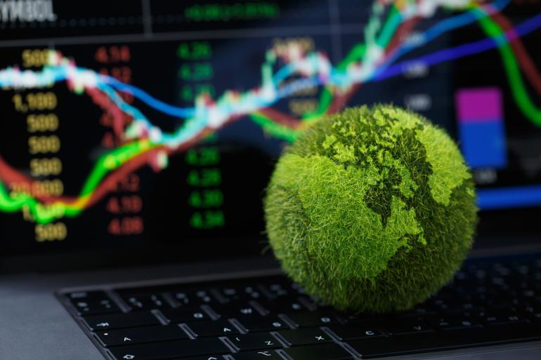 Green, grassy globe in front of a computer screen with stocks on it. 