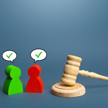 2 wooden-like figures, 1 red, 1 green, with checkmarks over heads, next to gavel