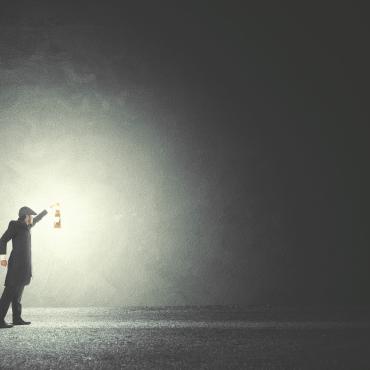 Man holding up a glowing lamp in the midst of darkness. 
