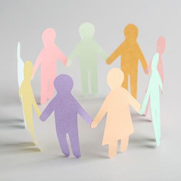 Paper cut outs of a diverse group of people holding hands in a circle. 