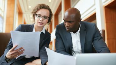 a female professional holding papers reviews documents with a male professional