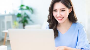 Smiling Asian woman typing on a laptop.