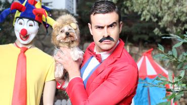 circus tent, clown, man, appears, white, holding dog, dressed like circus ringleader, his expression is like he is possibly in charge