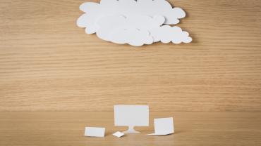 Paper cutout of computers under a cloud against a wooden table background. 