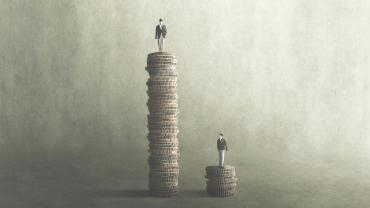 A man standing on a tall stack of coins next to a man standing on a smaller stack. 