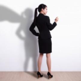 a standing woman in a suit with her shadow against a wall wears a superhero cape