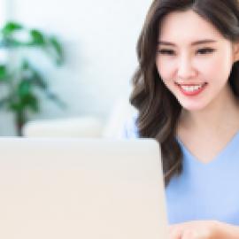 Smiling Asian woman typing on a laptop.