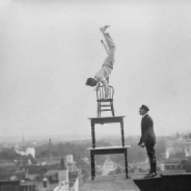 a man balancing in a handstand on top of stacked tables and chairs