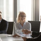 Smiling woman and man at boardroom table shaking hands 
