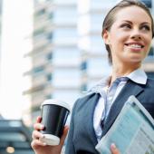smiling female professional in a city holding a coffee cup and work documents
