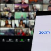 Phone with zoom logo in foreground, desktop zoom meeting in background