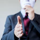 a business person with their hand held out to shake also holds a mask over their face, concealing their identity