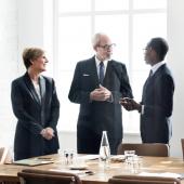 Group of diverse business people in sunny board room in front of a wood table.