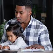 African American man working at home office with his toddler on his lap.
