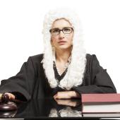 judge with gavel and book, at desk, wearing robe and British-style white wig, appears female/white