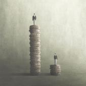 A man standing on a tall stack of coins next to a man standing on a smaller stack. 