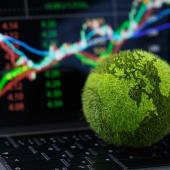 Green, grassy globe in front of a computer screen with stocks on it. 