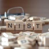 Scrabble pieces on a table. Four of them are stacked next to each other, spelling out "NIST."