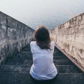 an image of a person sitting on stone steps leading to a body of water